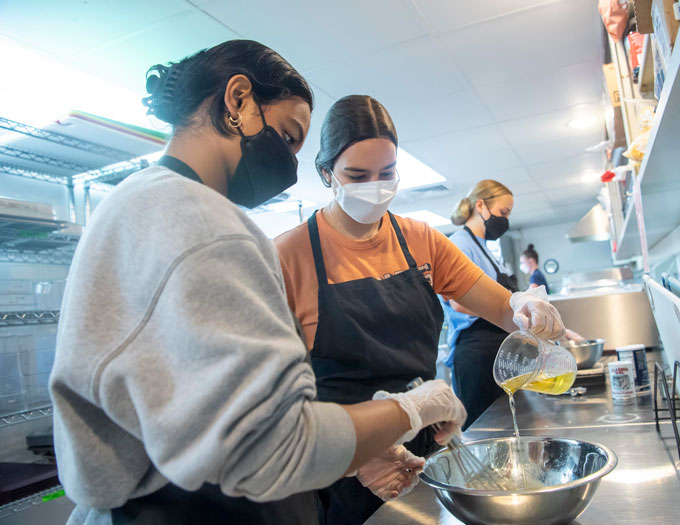 Students working in a kitchen and mixing ingredients in a bowl 
