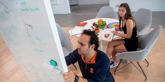 Instructor writing on a white board and assisting a student