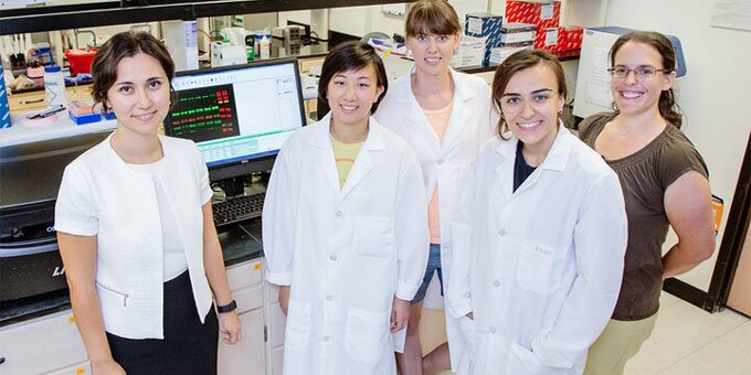 Group of students and instructors in a lab with white lab coats on