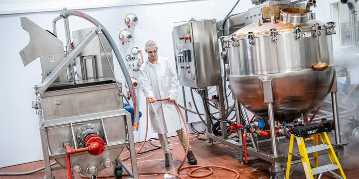 Student using a hose to clean floors next to three large machines.