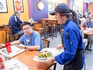 Student serving food to other students in cafe